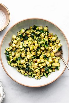 a white bowl filled with zucchini and spinach next to two spoons