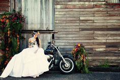 a woman in a wedding dress sitting next to a motorcycle with flowers on the side