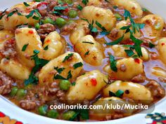 a white bowl filled with pasta and meat in a broth, garnished with parsley