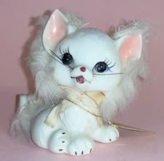 a white cat figurine sitting on top of a pink surface