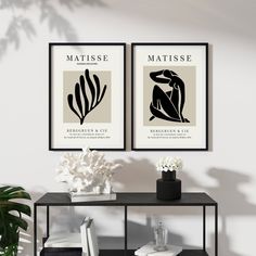 two black and white art prints on a wall above a table with flowers in vases