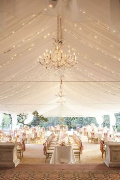 the inside of a tent with tables and chairs set up for a wedding reception under a chandelier