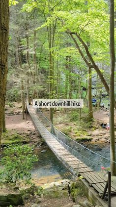 a short downhill hike sign on a bridge over a stream in the woods with people walking across it