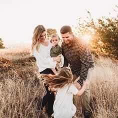 a family playing in the tall grass at sunset with their toddler holding his mom's hand