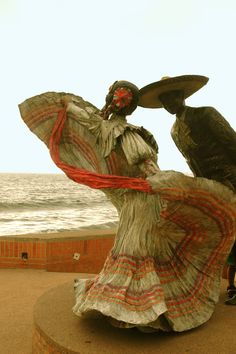 a woman in a long dress standing next to a bird on top of a statue