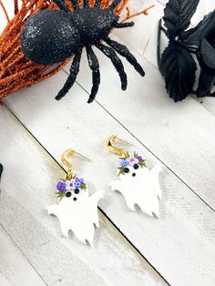 two white earrings with purple flowers on them and a spider hanging from the earwires