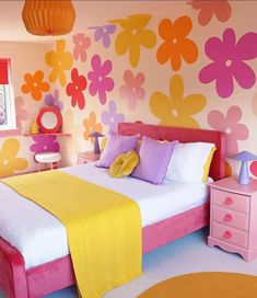 a bedroom decorated in pink, yellow and orange with flowers painted on the wall above the bed