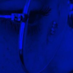 a woman's eye with long lashes is illuminated by blue light in the dark