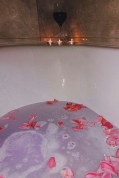 a bathtub filled with water and rose petals floating on the floor next to candles