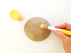 someone using a paintbrush to paint a piece of paper on a white surface next to a round object