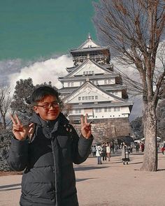 a woman standing in front of a tall building holding up two peace signs with her hands