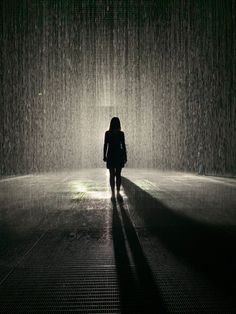 a woman standing in the rain with her back turned to the camera and light shining down on her