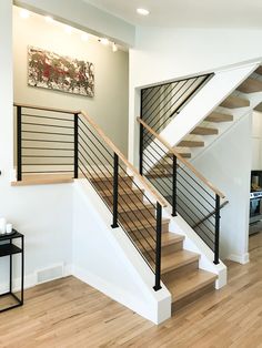 there is a stair case in the middle of this living room with wood floors and white walls