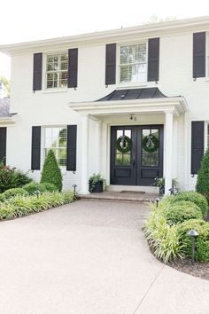 a large white house with black shutters on the front door and two wreaths