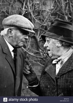 an old man and woman standing next to each other in front of a brick wall