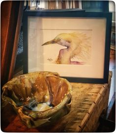 a bird is sitting in a bowl next to a framed print on a table top