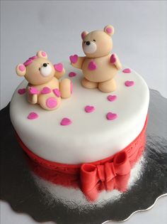 two teddy bears sitting on top of a white cake with pink and red icing