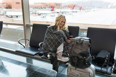 a woman sitting on a bench next to luggage and looking at her phone in an airport