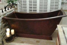 an old fashioned bathtub in a bathroom with candles on the floor and brick walls