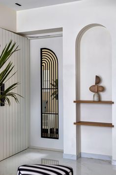 a white room with a black and white striped ottoman next to a tall wooden shelf