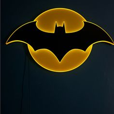 a neon batman sign hanging from the side of a dark wall with a yellow light