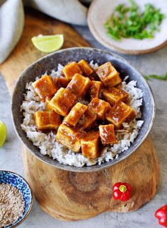 a bowl filled with rice and tofu on top of a wooden cutting board