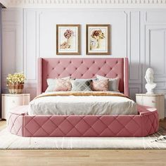 a pink bed in a bedroom with white walls and wooden floors, along with two framed pictures on the wall