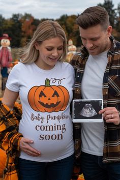 a man and woman standing next to each other in front of pumpkins with the baby pumpkin coming soon t - shirt on