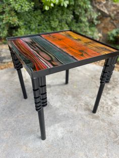 a small table made out of wood and metal legs with colorful paint on the top