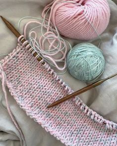 two balls of yarn and knitting needles on top of a white sheet with pink crochet