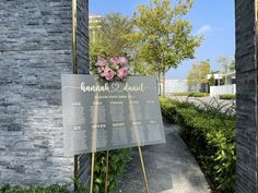 a memorial sign with flowers on it in front of a brick wall and stone pillars