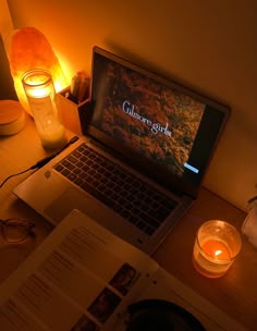 an open laptop computer sitting on top of a desk next to a candle and book