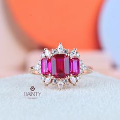 a pink tourmaline and diamond ring sitting on top of a white surface with an orange ball in the background