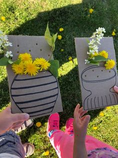 two people are holding up small vases with flowers in them on the grass outside