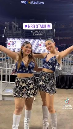 two young women standing next to each other in front of a stage with their arms up