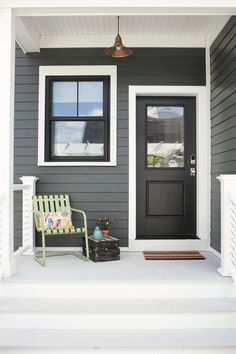 the front door of a gray house with white trim and black shutters is flanked by a green bench