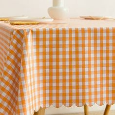 an orange and white checkered table cloth with scalloped edge on wooden legs