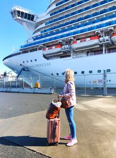 a woman standing in front of a cruise ship holding a suitcase and looking at the ocean