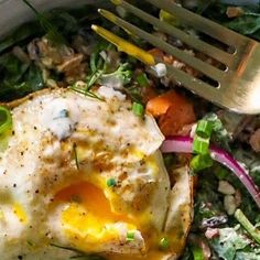 an egg is sitting on top of a bed of greens and carrots next to a fork