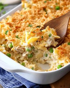 a casserole dish filled with chicken and peas, topped with a wooden spoon