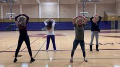 four girls are doing exercises on the basketball court while holding their hands in the air