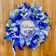 a blue and white welcome wreath hanging on a wooden fence