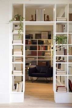 an open book shelf filled with books next to a black chair and white shelves full of books