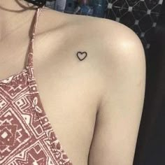 a woman with a small heart tattoo on her left shoulder and right arm behind her back