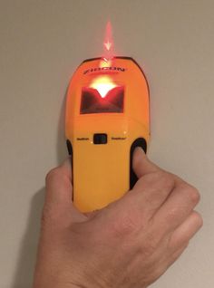 a hand holding a yellow device with red light on it