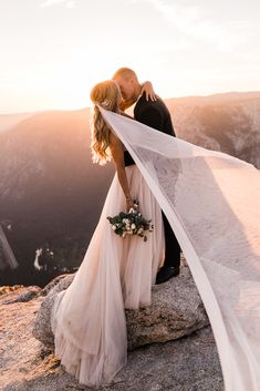 a bride and groom kissing on top of a mountain