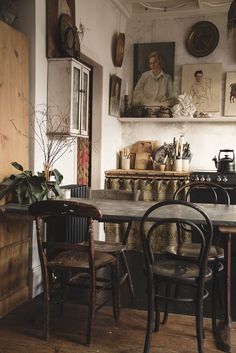 an old fashioned kitchen table and chairs in front of a wall with pictures on it