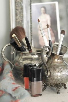 a silver vase filled with makeup brushes and other items next to an image of a woman's face