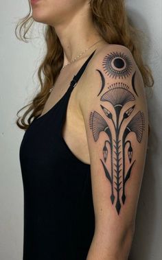 a woman with a black and grey tattoo on her arm, standing in front of a white wall