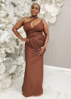 a woman standing in front of a christmas tree wearing a brown dress with one shoulder